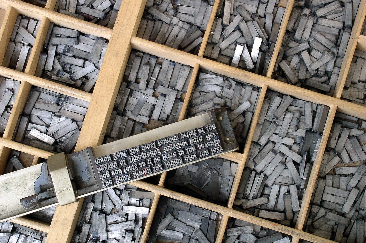 A wooden type case full of metal type, with a composing stick holding several set lines resting across it